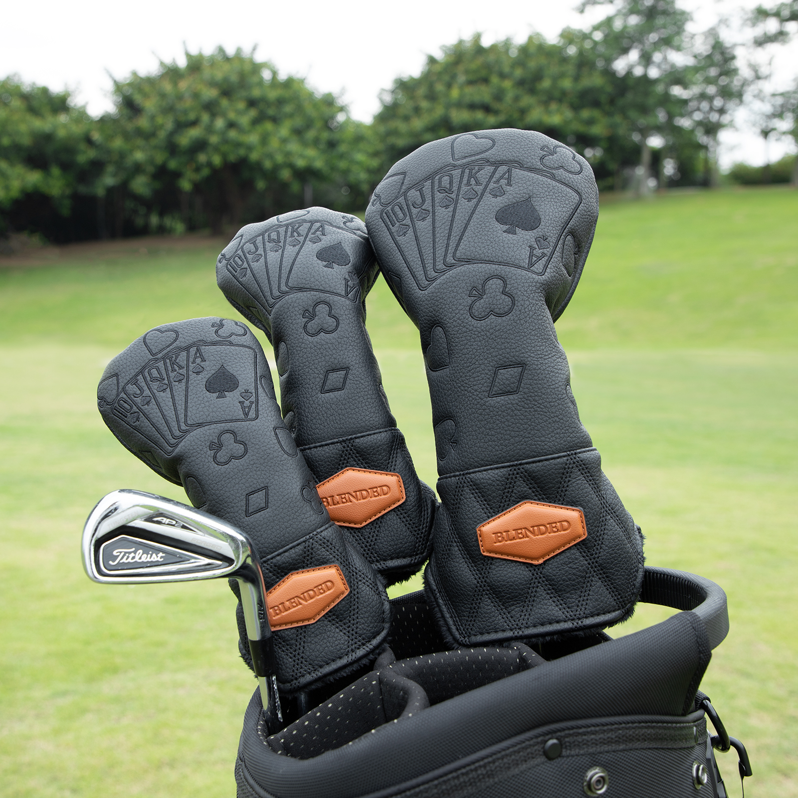 Three black covers with embossed card motifs sit in a golf bag on a grassy course.