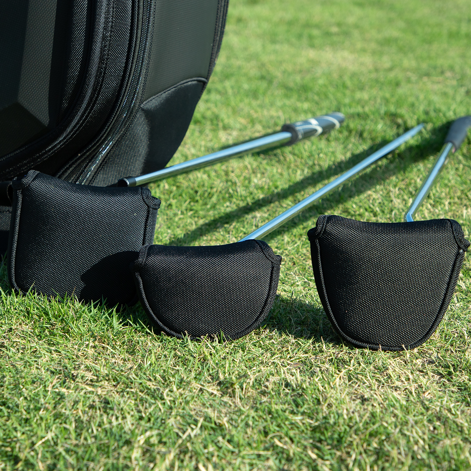 Three black covers sit on putter heads over grass, with the shafts extending across the image.