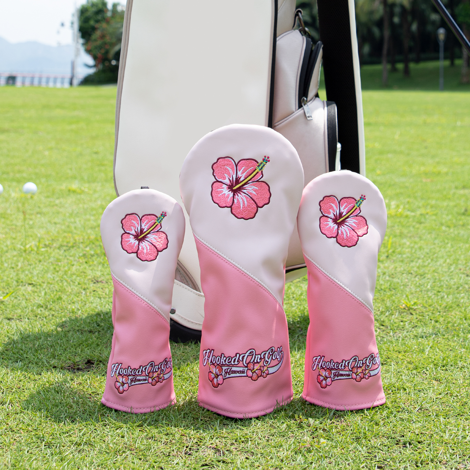 Three pink hibiscus covers stand beside a golf bag on a grassy course.
