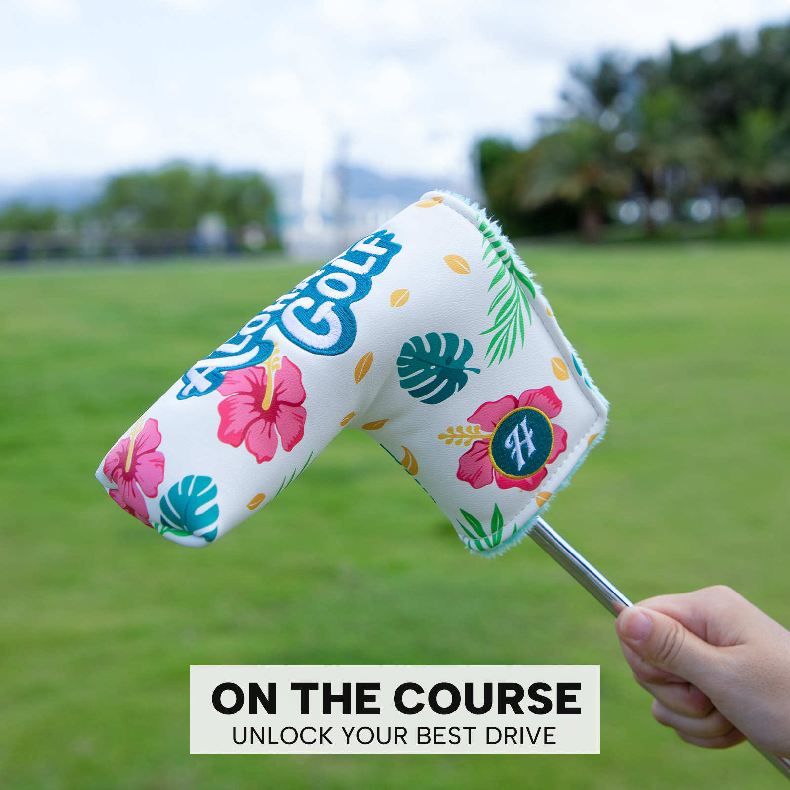 A hand holds the tropical-print cover over grass beneath the visible image caption “ON THE COURSE UNLOCK YOUR BEST DRIVE.”