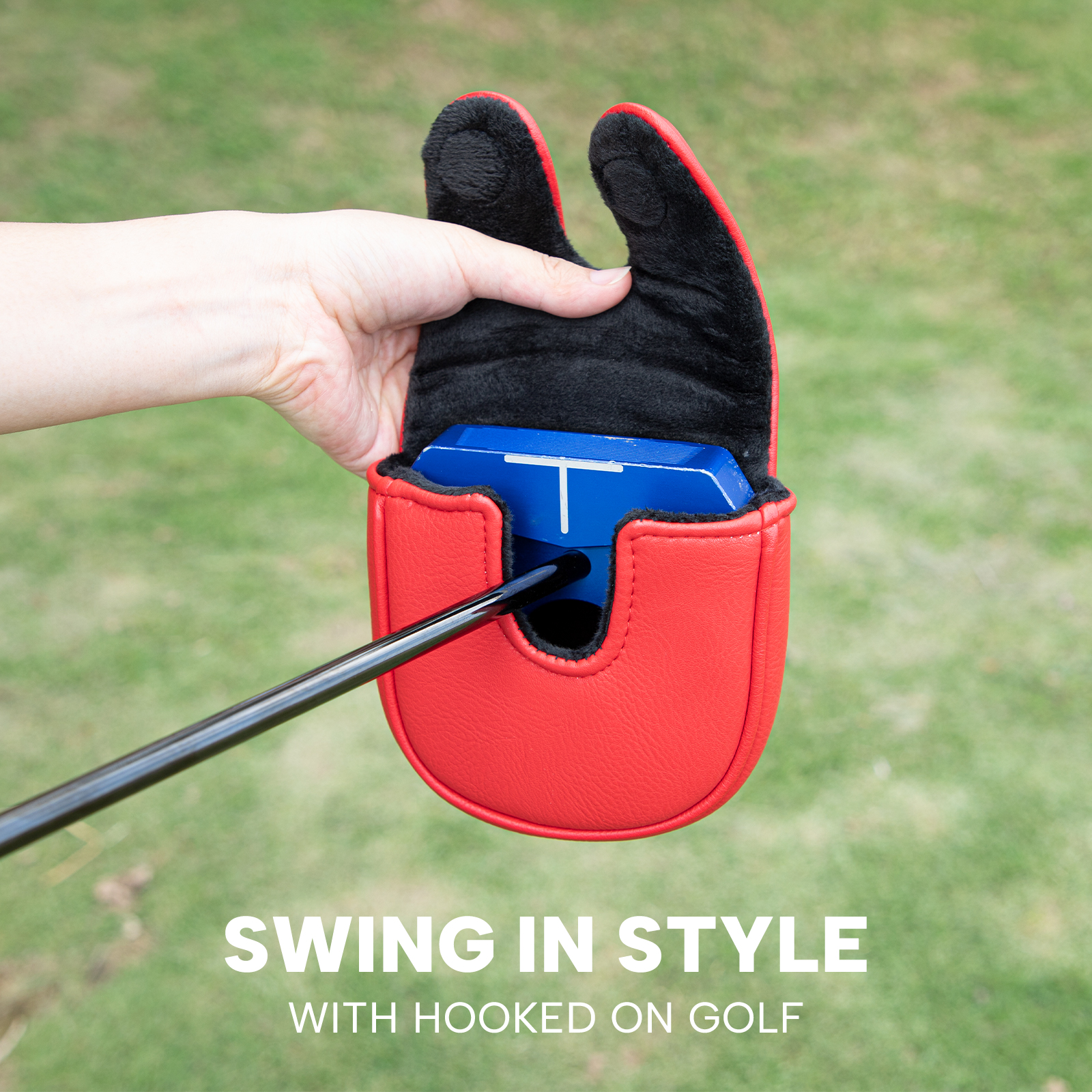 A hand holds open the red cover around a blue club head on grass beneath the visible text “SWING IN STYLE.”