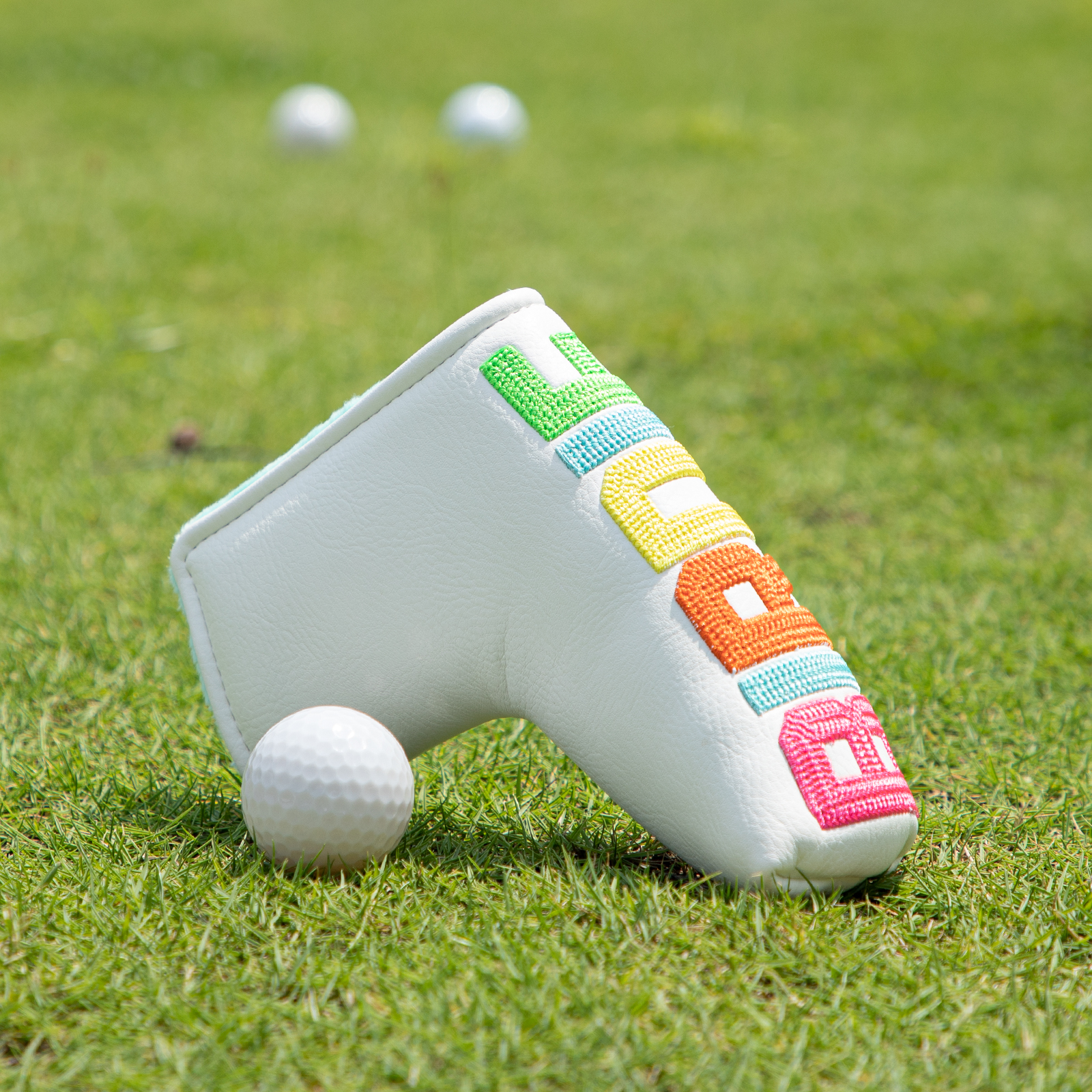 The white cover with colorful lettering rests on grass beside a golf ball.