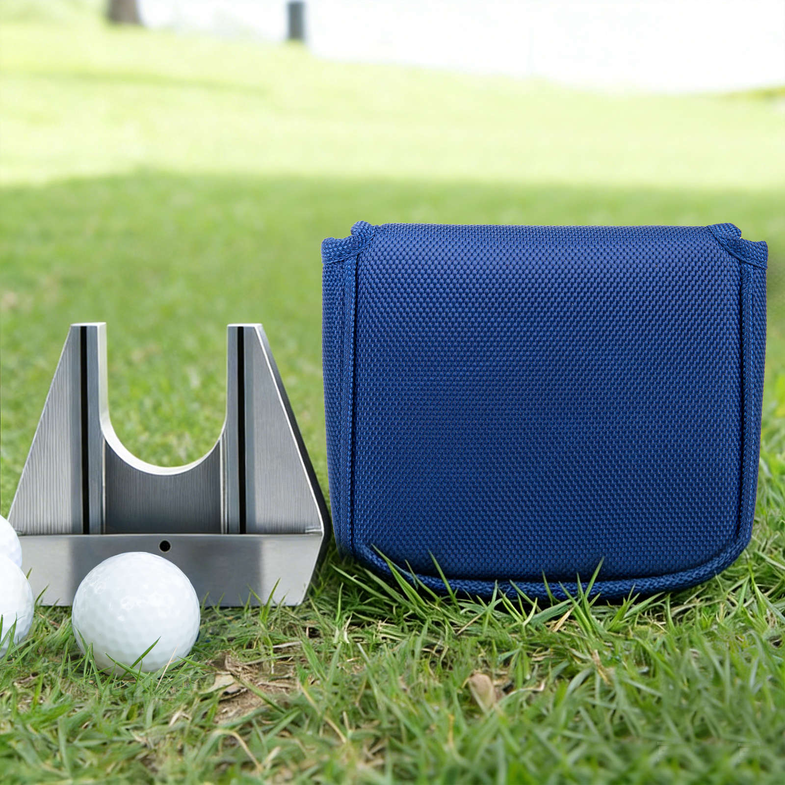 A blue cover stands beside a metal putter head and white golf ball on grass.